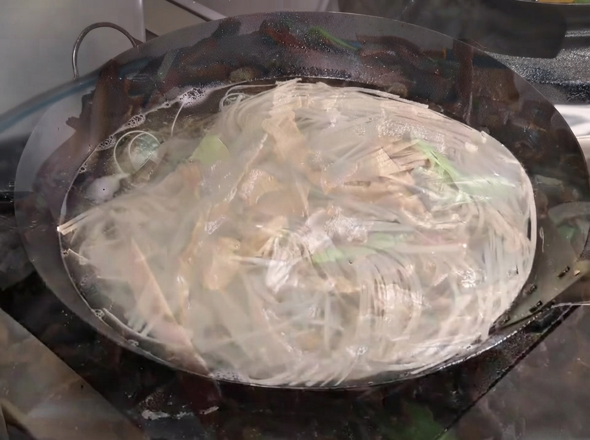 Noodles boiling vigorously in a large wok filled with water.