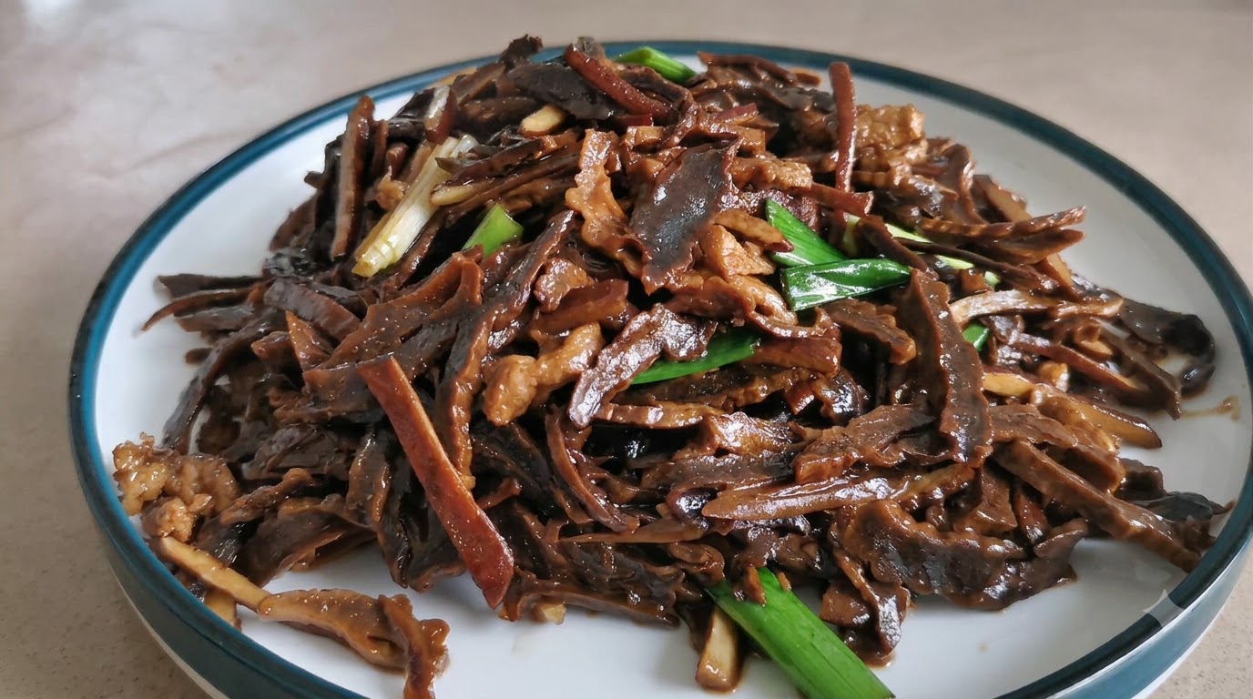 A plate of savory stir-fried shredded dried bamboo shoots and pork garnished with green garlic shoots