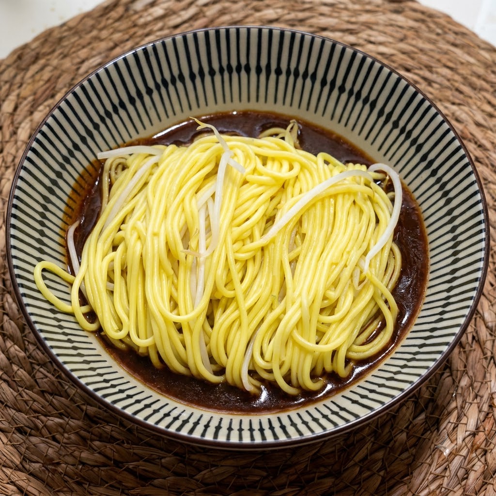 A portion of hot, cooked yellow noodles sitting in a patterned ceramic bowl over a rich, dark brown sauce.