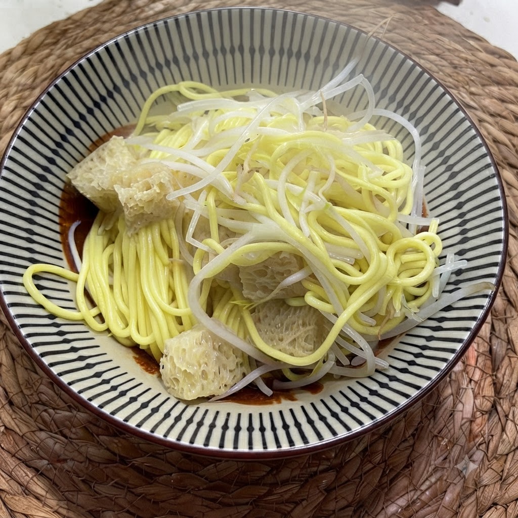 Cooked yellow noodles in a bowl topped with pale mung bean sprouts and textured pickled vegetables.
