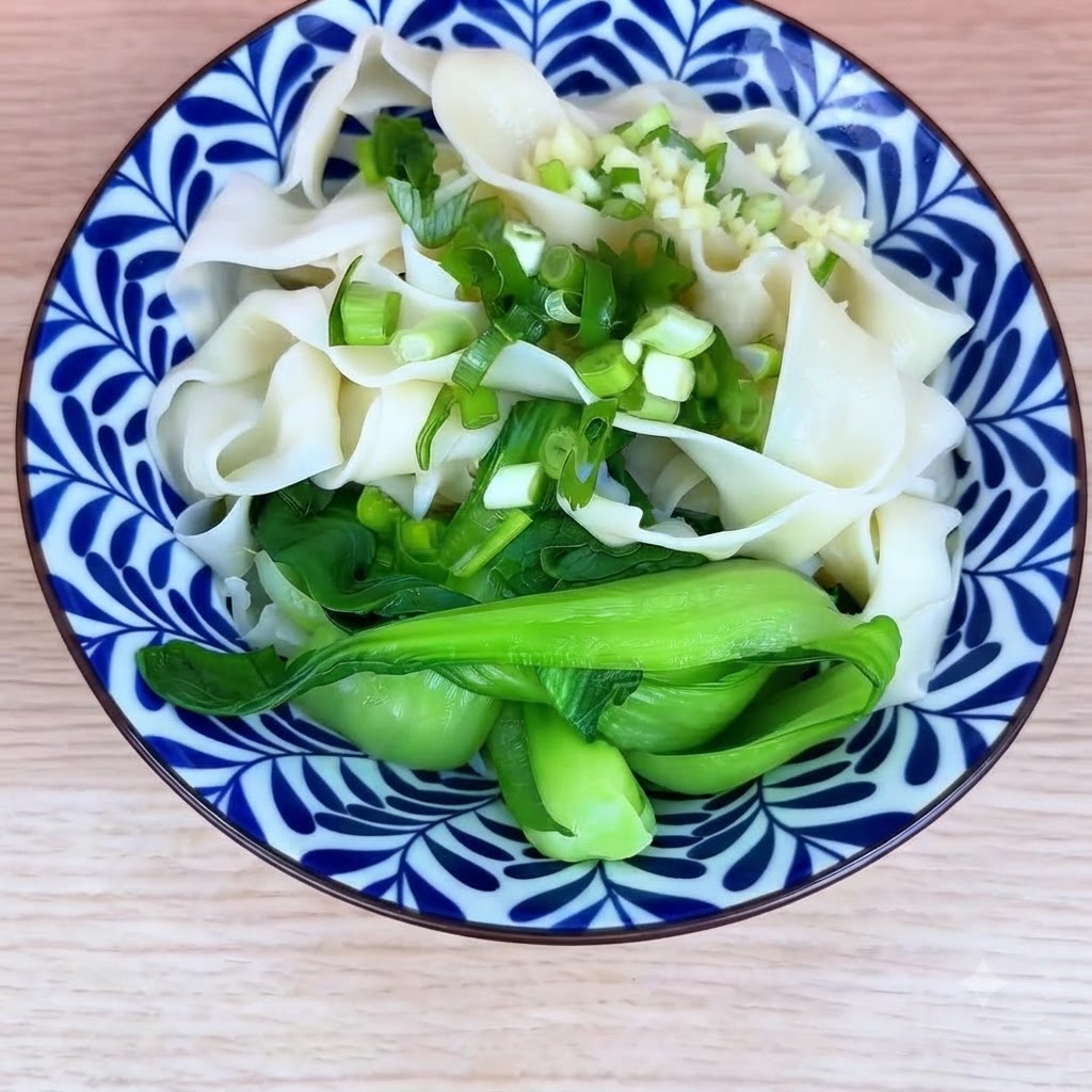 A bowl of cooked noodles and bok choy topped with chopped green onions and minced garlic.