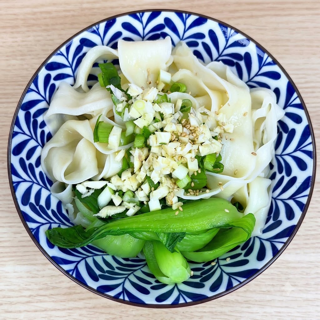 White sesame seeds and spices sprinkled on top of the garlic and noodles in a bowl.