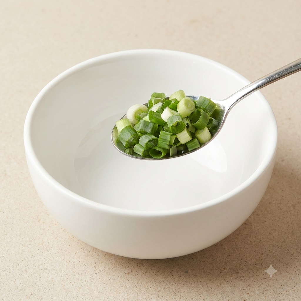 A metal spoon filled with freshly chopped green spring onions held above a white bowl.