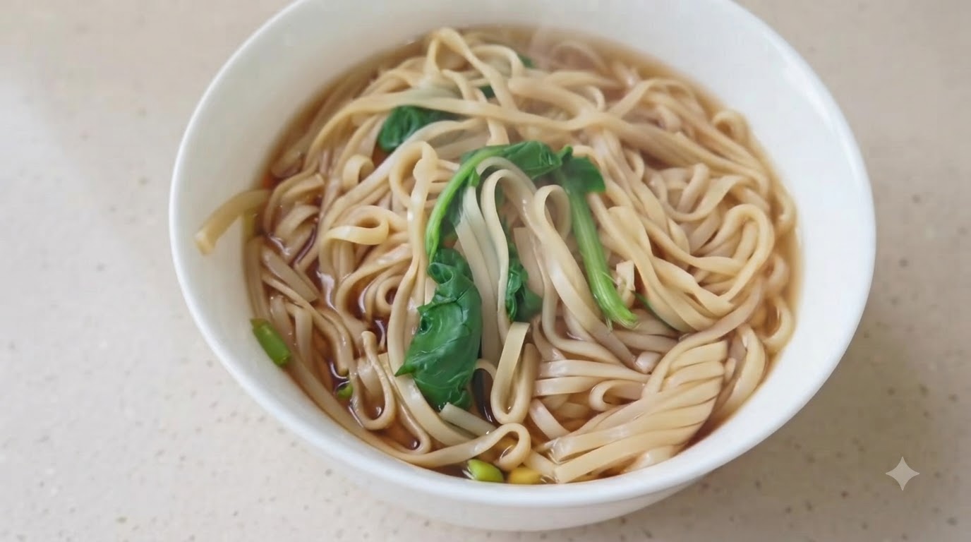 A bowl of simple soy sauce noodles in a light broth, garnished with leafy greens