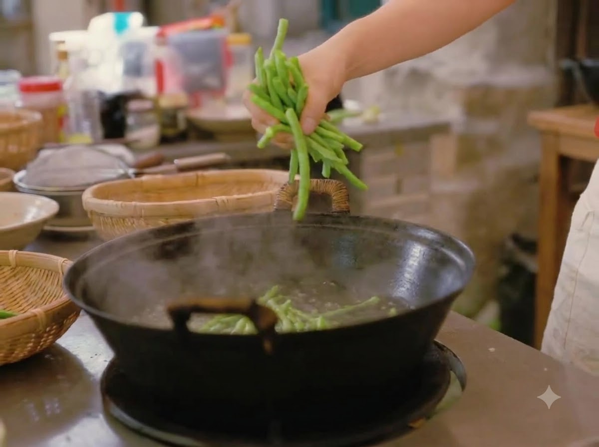 A hand dropping a bunch of fresh green beans into a large wok of boiling water.
