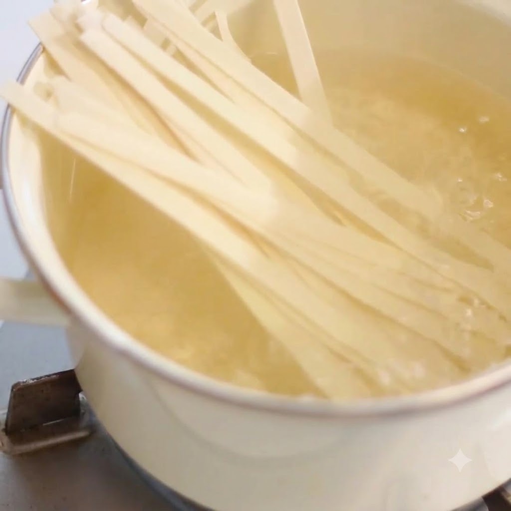 Wide noodles cooking inside a boiling pot of hot water on a stovetop.