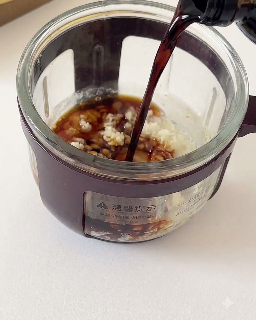 Dark soy sauce being poured from a bottle into a glass container filled with minced garlic and seasonings.