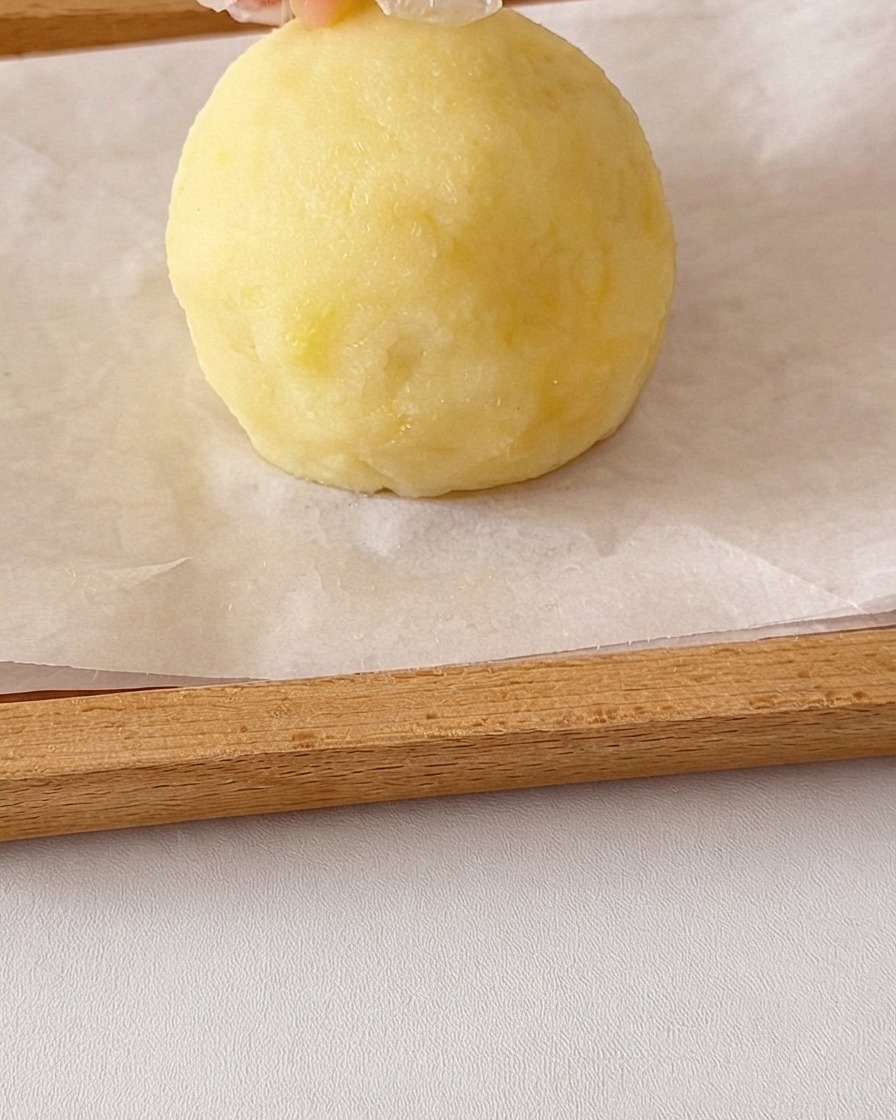 A round ball of smooth mashed potato being shaped by hands with small potato pieces added on top for ears.
