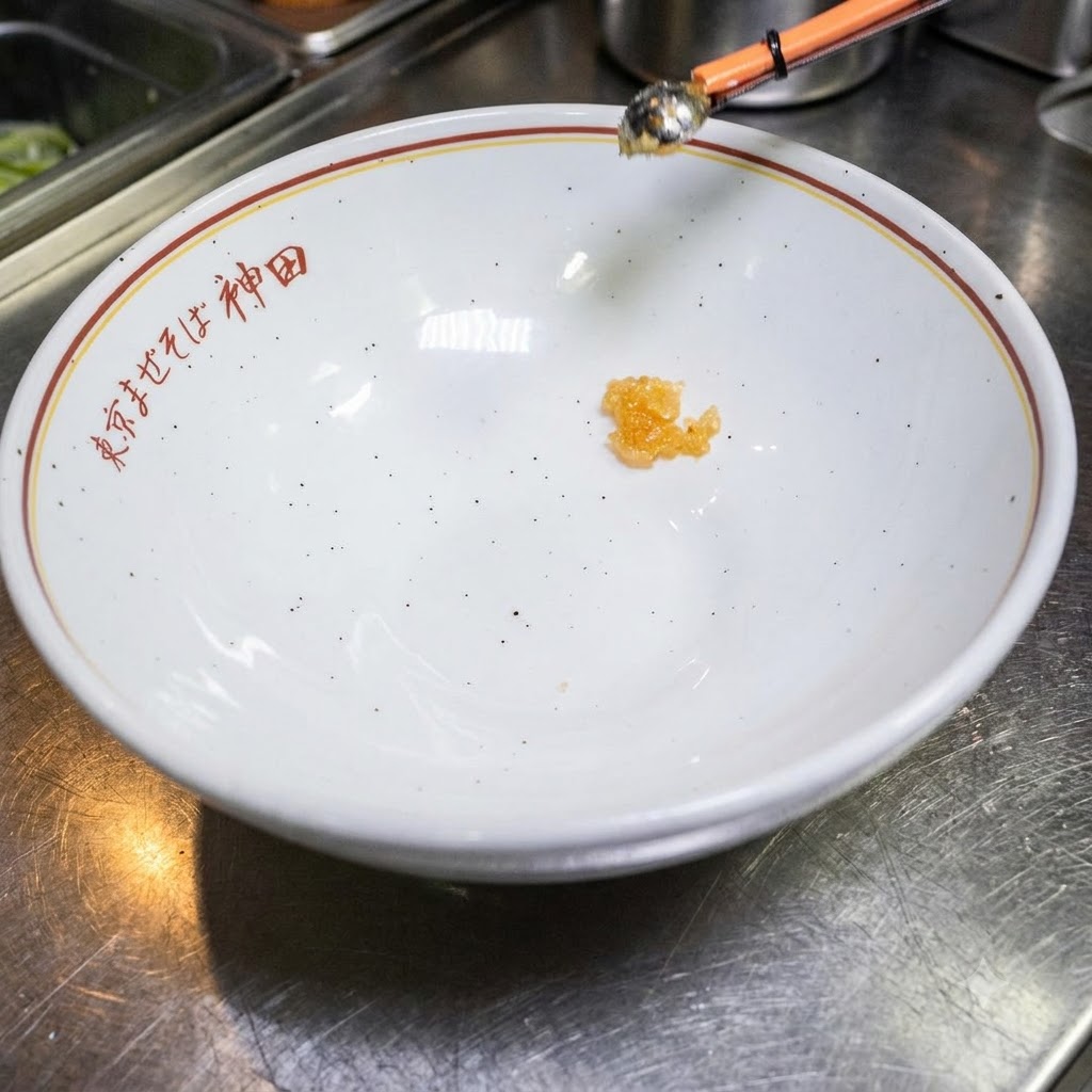 A small amount of seasoning liquid sitting at the bottom of an empty white bowl with Japanese text.