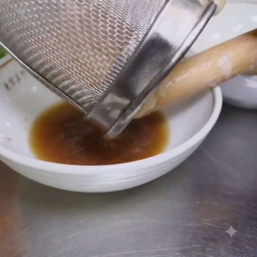 Boiled ramen noodles being poured from a mesh strainer into a bowl containing seasoning.