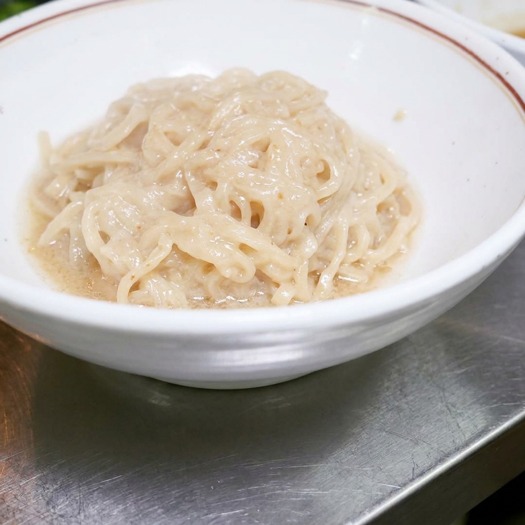 Cooked ramen noodles sitting neatly inside a white bowl, ready to be mixed with the sauce.