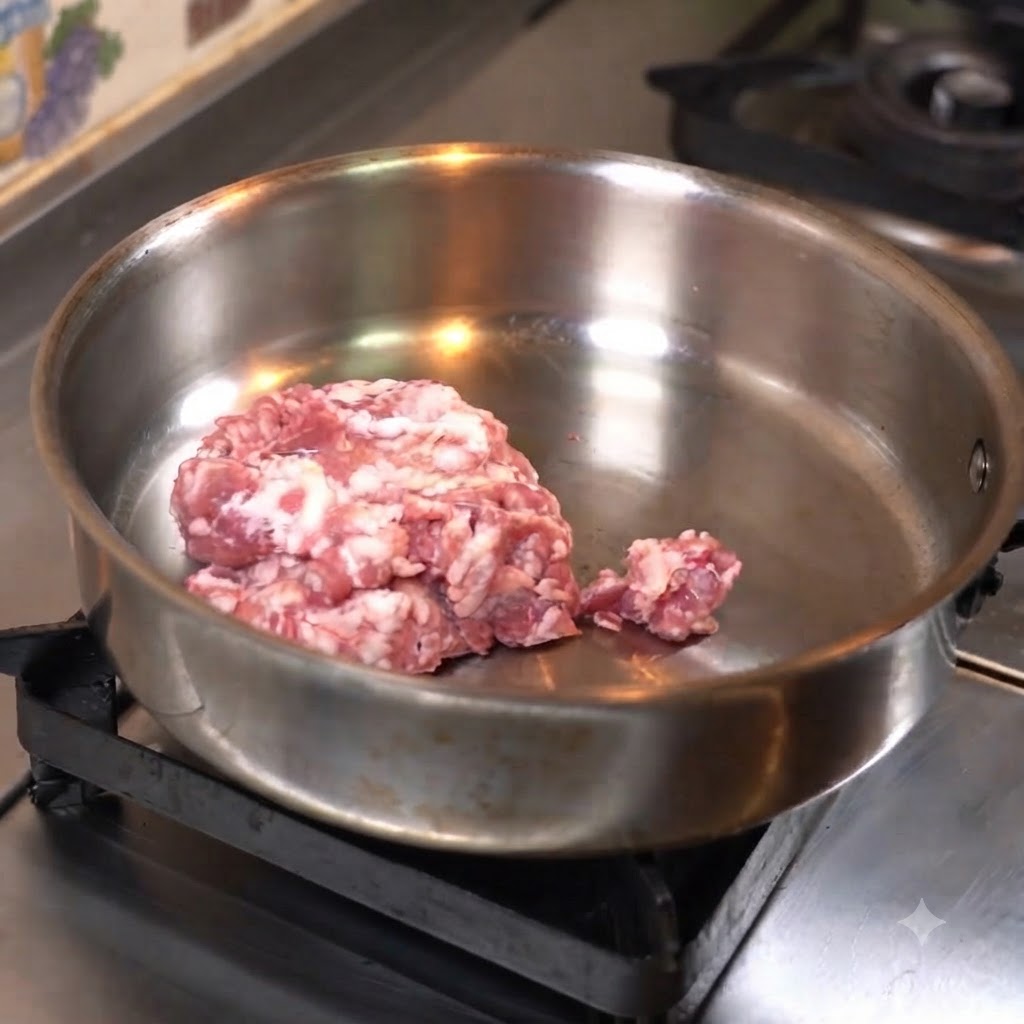 Minced meat being pressed flat into a stainless steel pan to cook.
