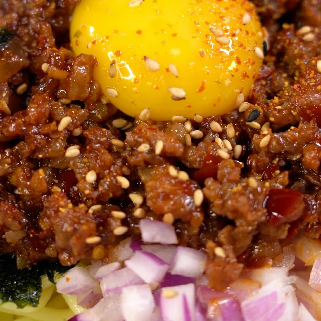 Sauce being poured and stirred into browned minced meat in a skillet.