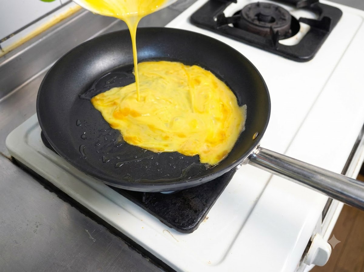 Beaten yellow eggs being poured from a container into a hot frying pan containing oil.