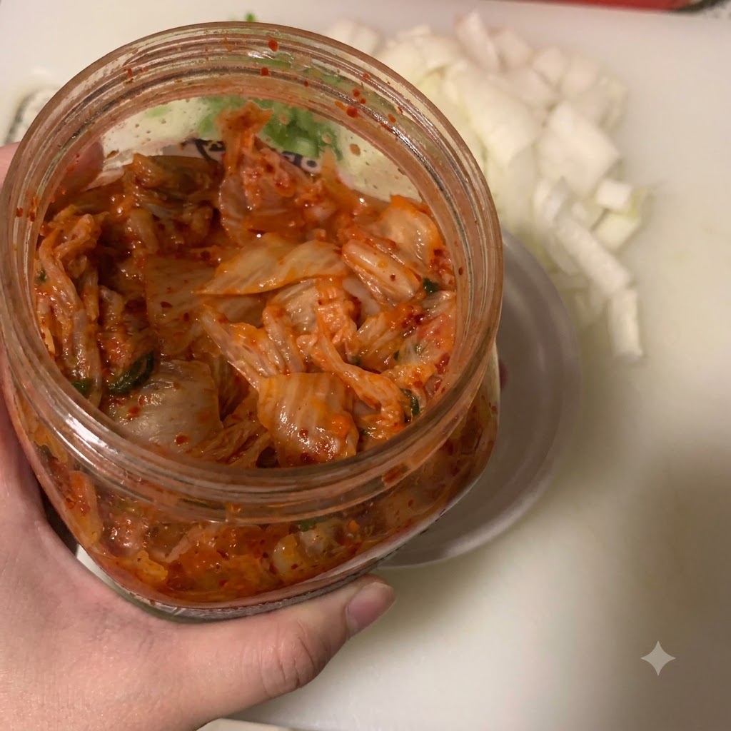 Kimchi being scooped into a small white bowl with a spoon next to a container of chopped onions.