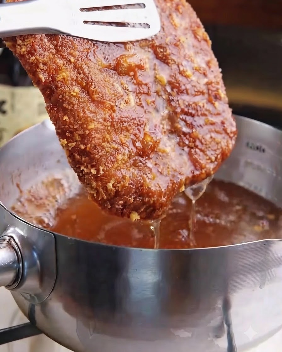 A crispy golden-brown fried pork cutlet being lifted out of hot frying oil with tongs.