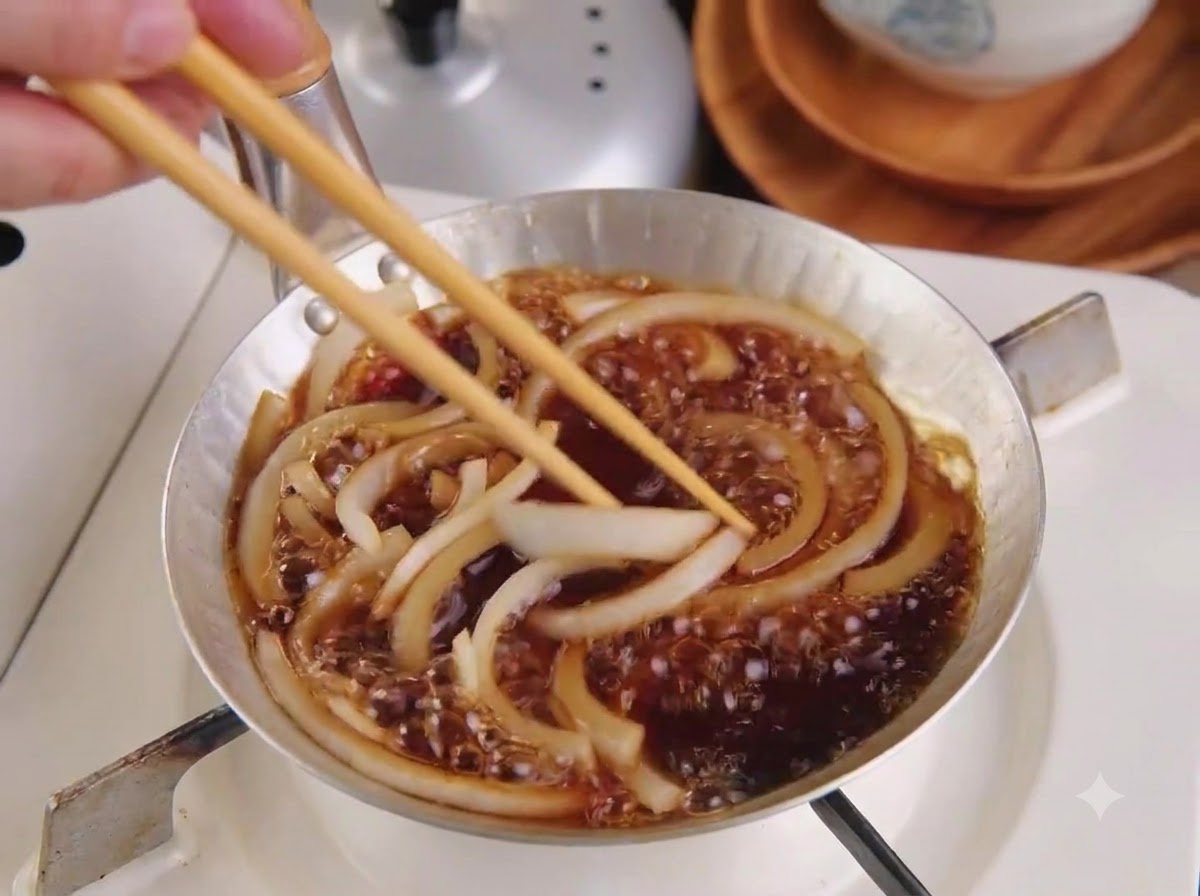 A sliced pork cutlet being placed into a pan on top of simmering onions and sauce using wooden chopsticks.