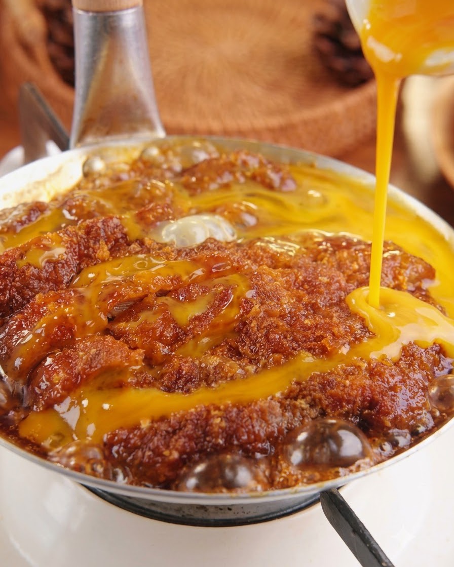 Yellow beaten egg mixture being poured from above onto the simmering pork cutlet inside a pan.