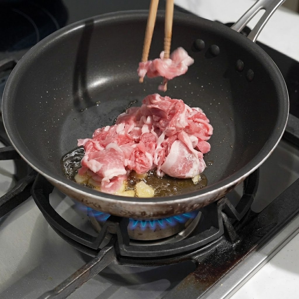 Raw thinly sliced pork being placed into a pan with hot oil and frying garlic using chopsticks.