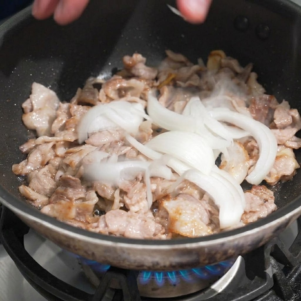 Sliced white onions being dropped by hand into a pan of cooked sliced pork.