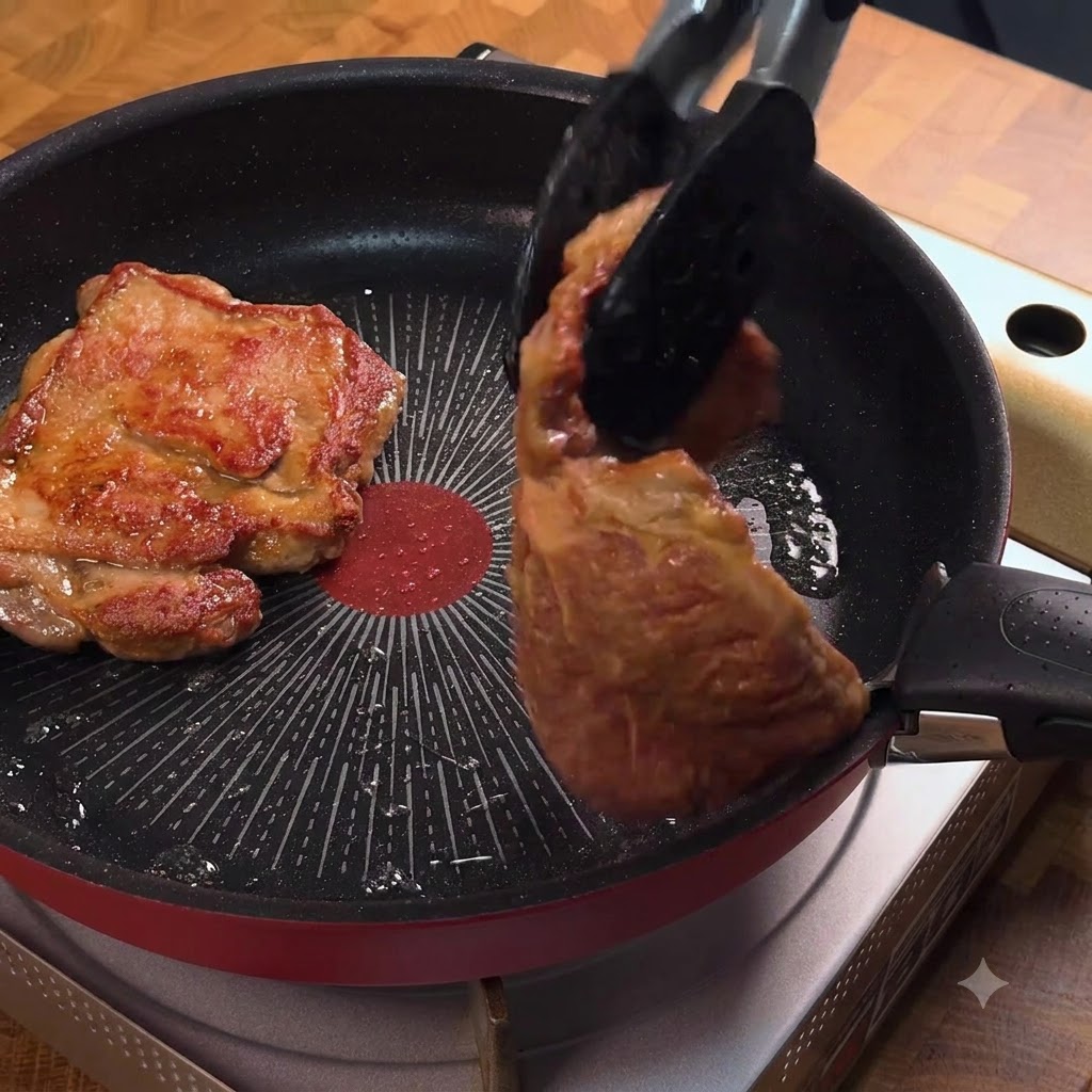 Tongs flipping a golden-brown pork chop in a frying pan.