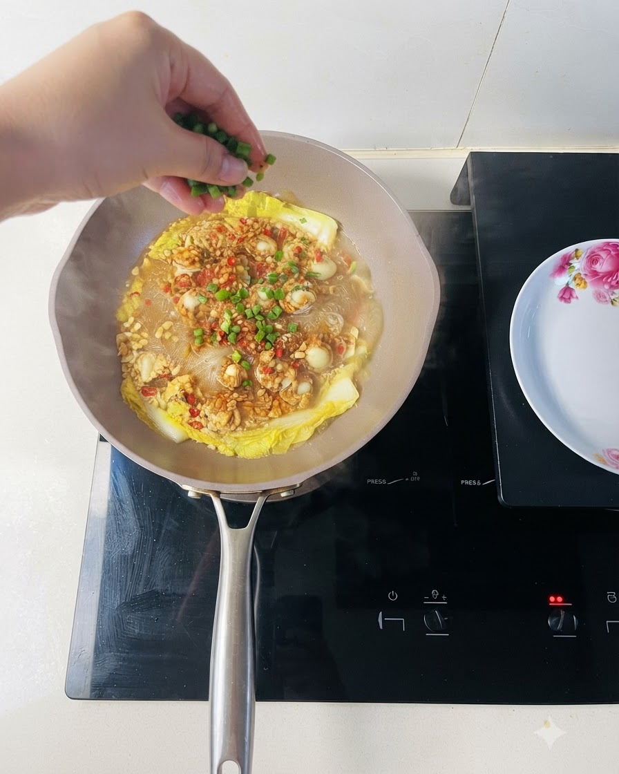 Freshly chopped green onions being sprinkled over a pan of cooked scallops and vermicelli noodles.