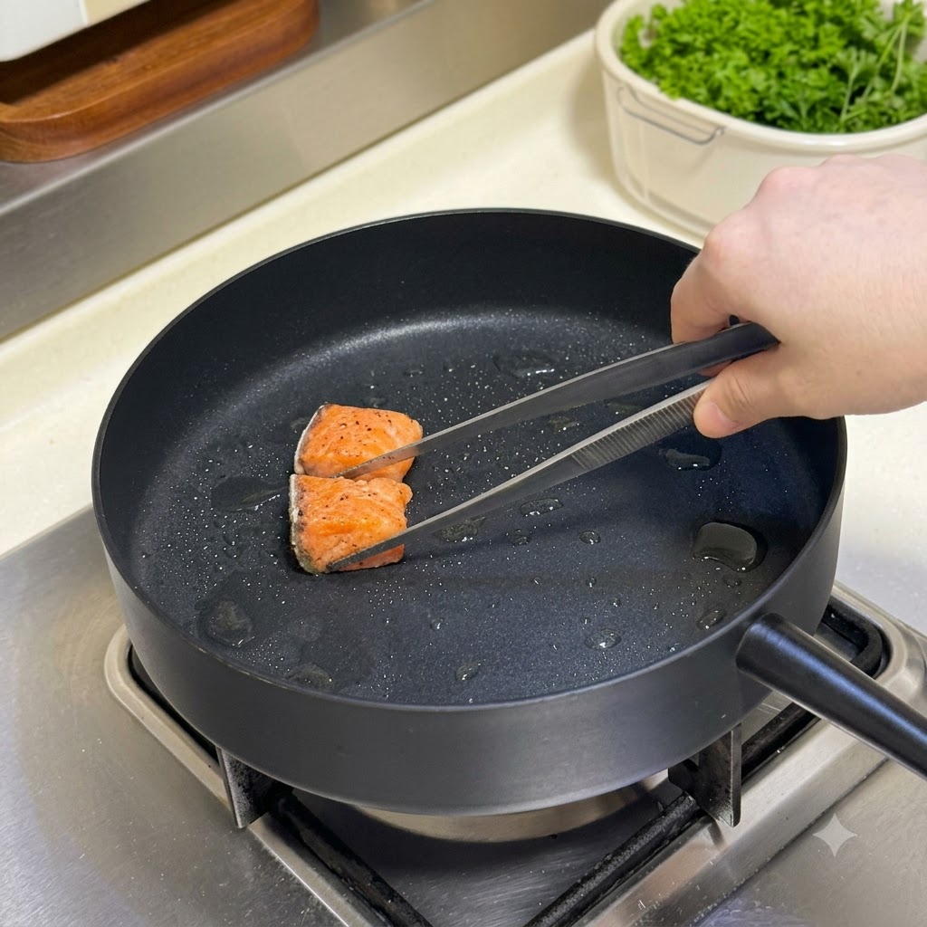 Seasoned salmon cubes being turned in a hot frying pan with a pair of tongs.