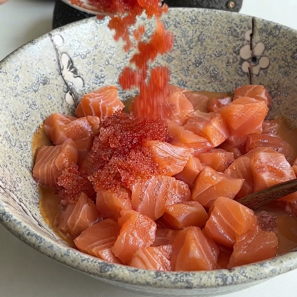 Bright red fish roe being poured from a spoon into a ceramic bowl filled with diced salmon and sauce.