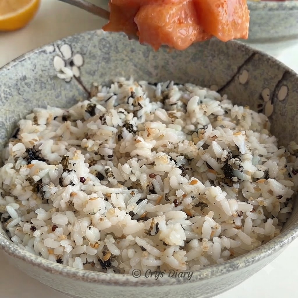 A spoonful of salmon mixture being placed over a ceramic bowl filled with white rice and seaweed flakes.