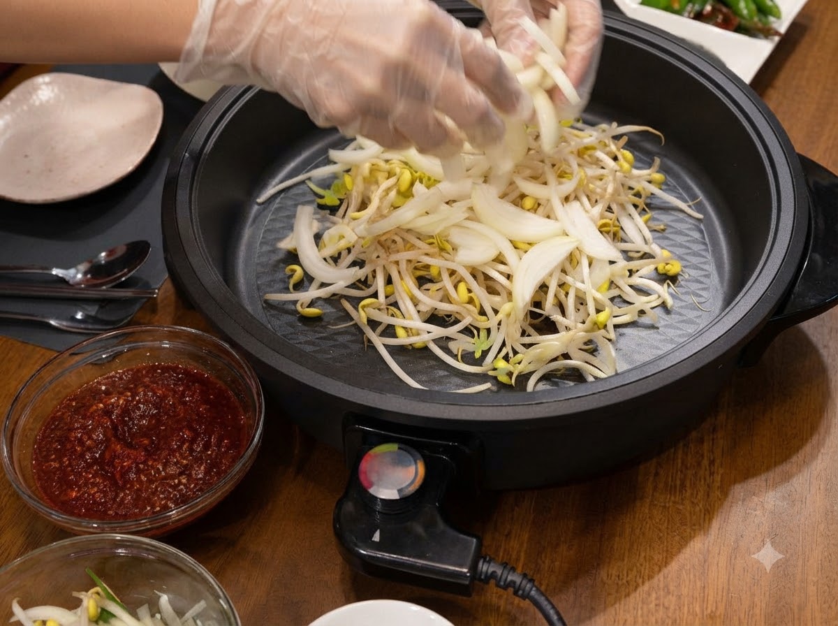 Gloved hands placing sliced onions into the electric skillet over bean sprouts.