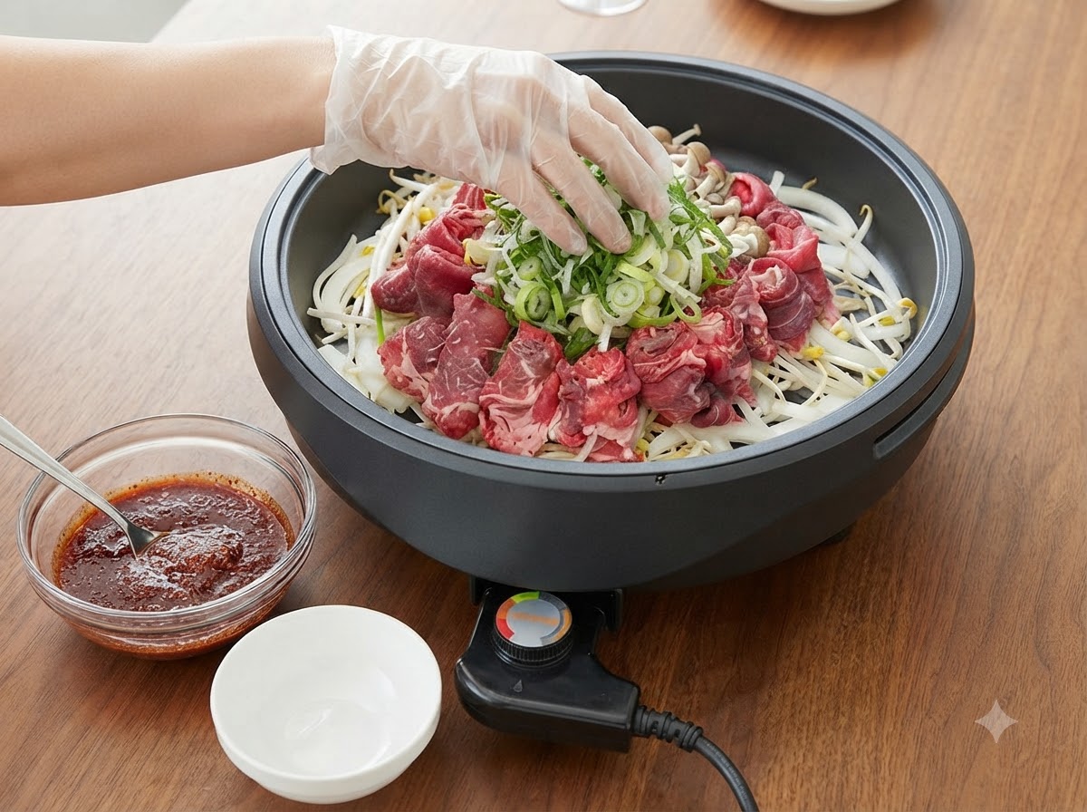 Gloved hands placing freshly shredded green scallions directly onto the center of the meat and vegetables in the pan.