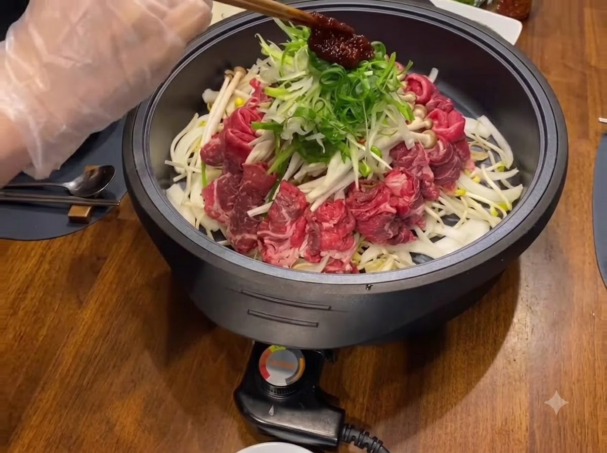 A dollop of dark red seasoning sauce placed on top of shredded green onions and meats in a black cooking pan.
