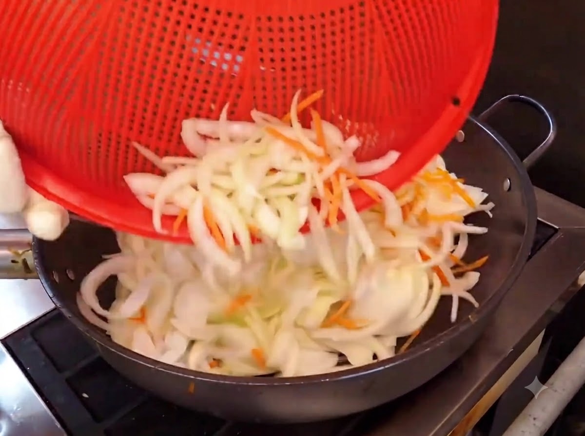 Onion and carrot shreds being poured from a red basket into a hot wok for stir-frying.