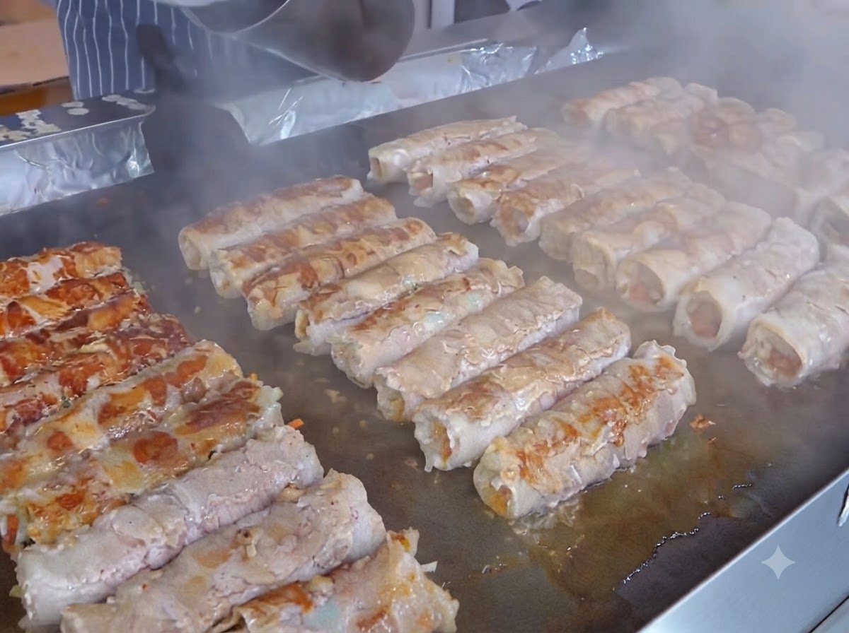 A yellow cheese slice being placed on top of the kimchi layer over the prepared meat rolls.