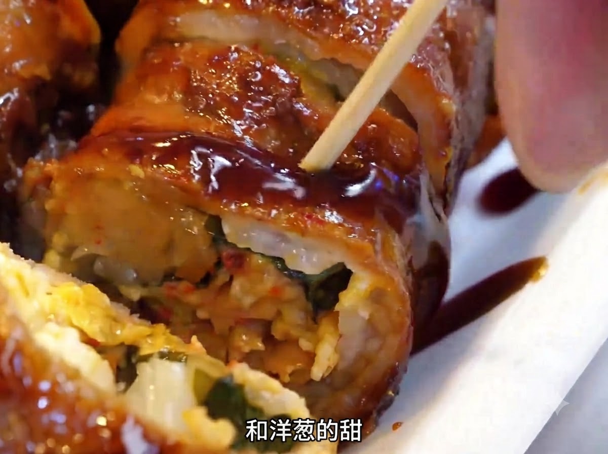 Meat rolls being flipped on the hot iron plate using a metal spatula.