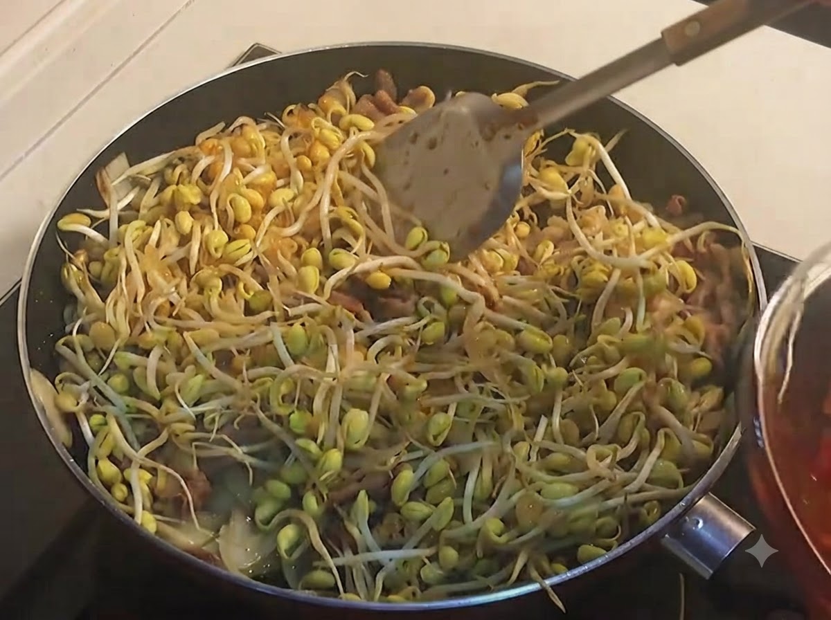 A ladle spooning dark red spicy sauce over a full pan of yellow soybean sprouts.