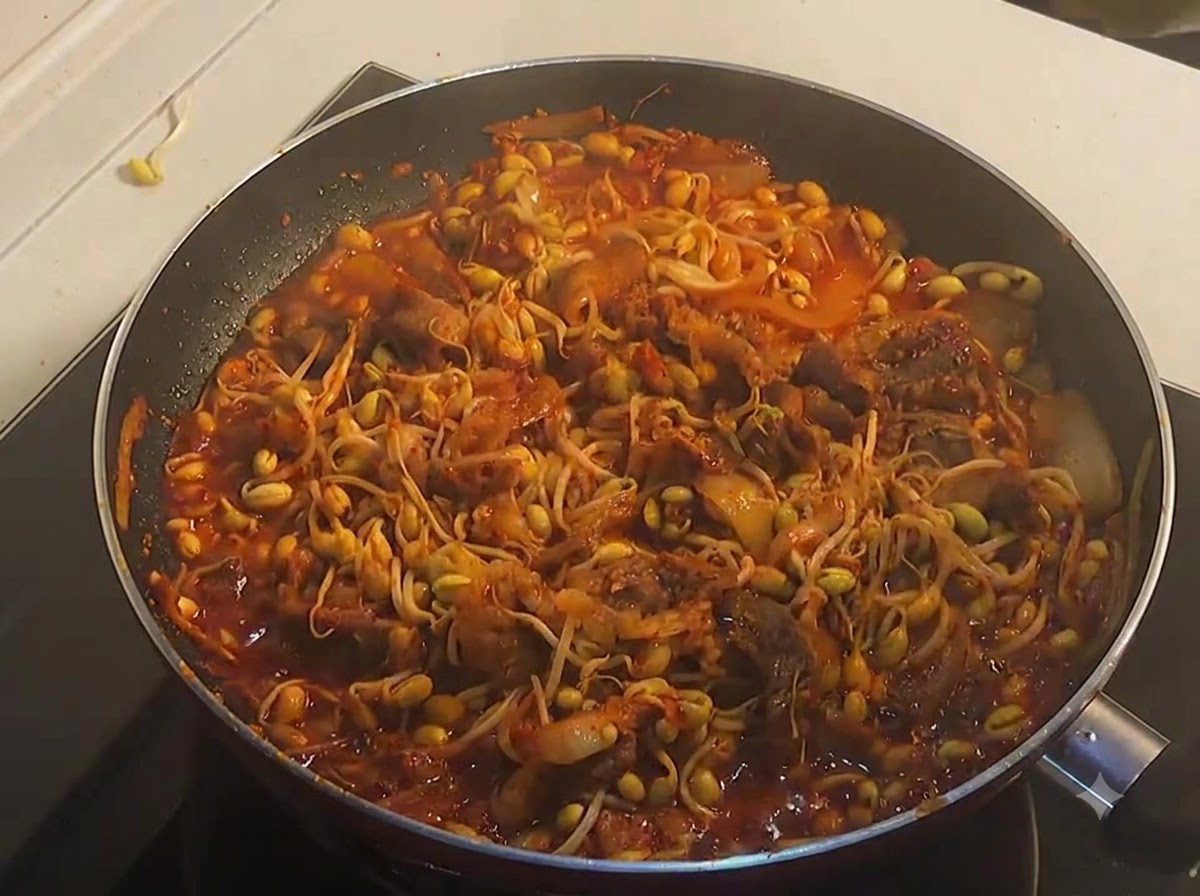 A pan full of fully cooked, bubbling spicy beef and yellow soybean sprouts in a rich red sauce.