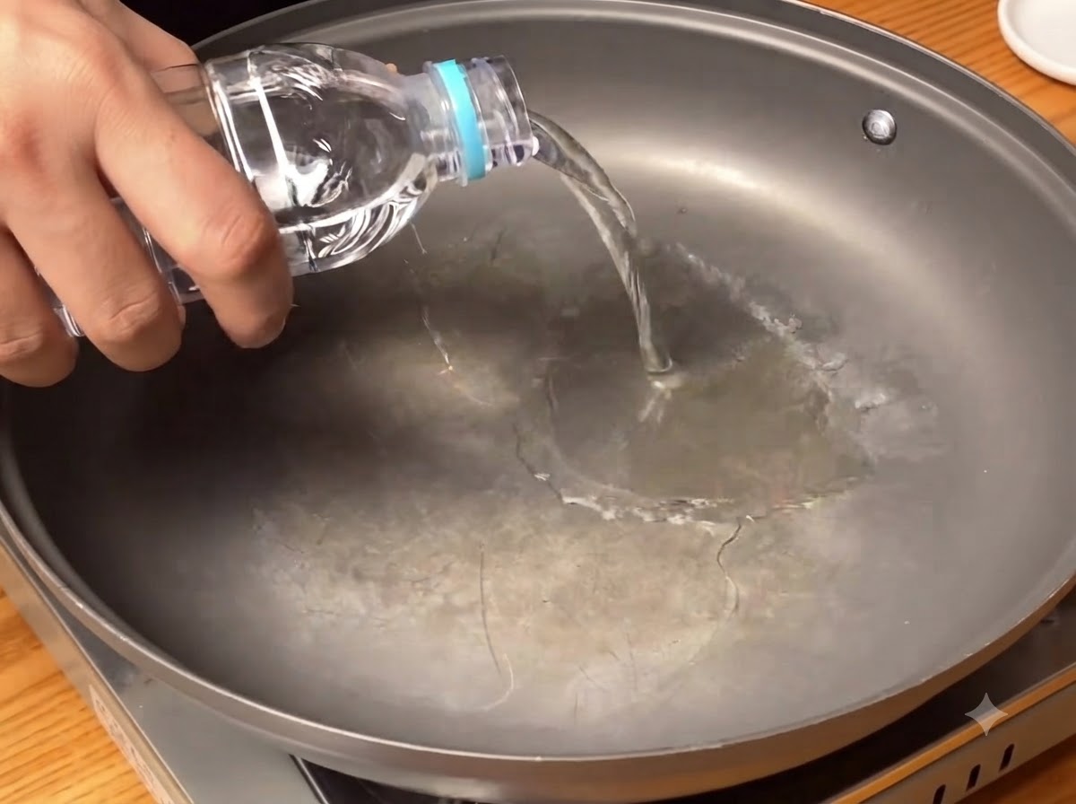 Clear water being poured from a bottle into the bottom of a wide cooking pan.