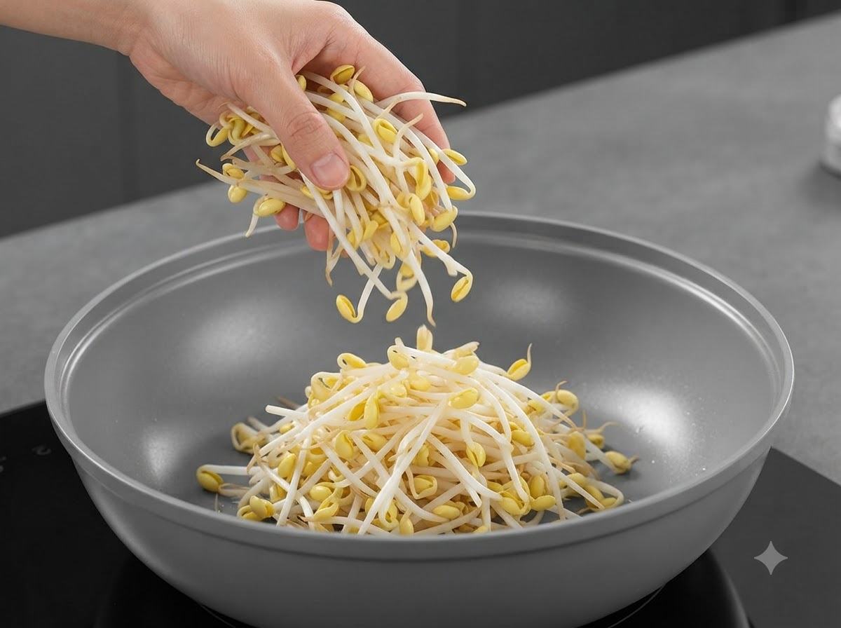 Fresh soybean sprouts being dropped from a hand into the center of the pan.
