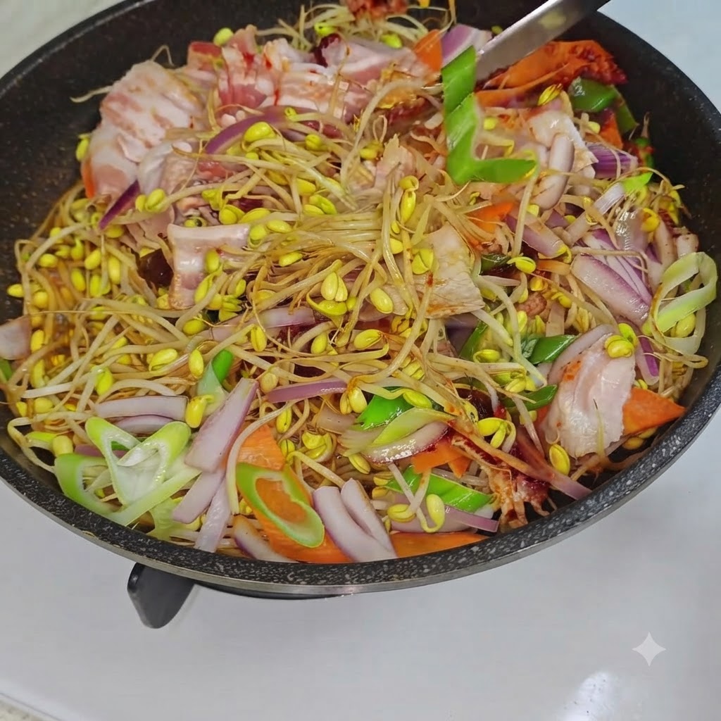 A cooking utensil stirring the mixed bean sprouts, pork belly, and vegetables inside a pan over heat.