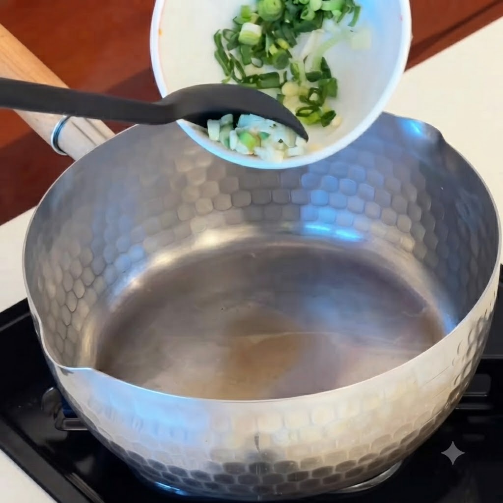 Sliced garlic, red kimchi pieces, and sausage rounds being tipped from a bowl into a heated pot.