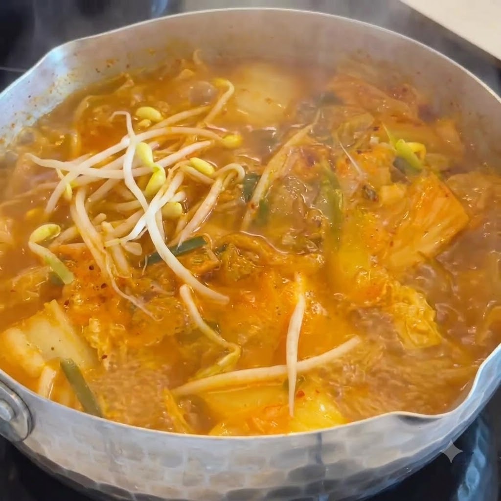 Crisp white bean sprouts being dropped into a simmering pot of orange kimchi and sausage soup.