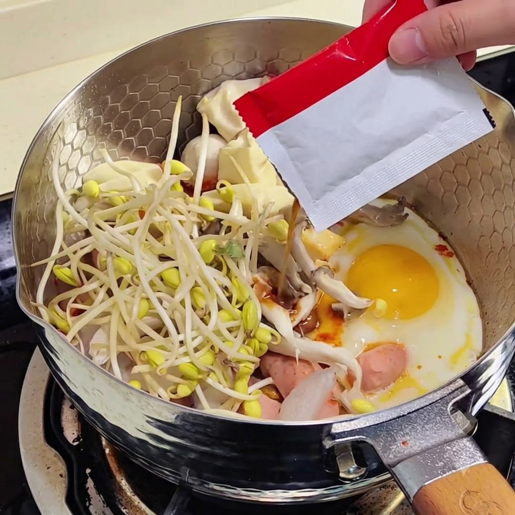 Bean sprouts in the pan with seasoning powder being poured from a red packet.