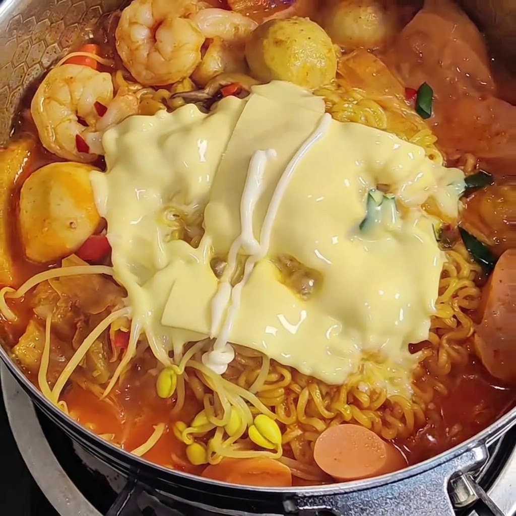 Mayonnaise being drizzled in a zigzag pattern over melted cheese on top of ramen.