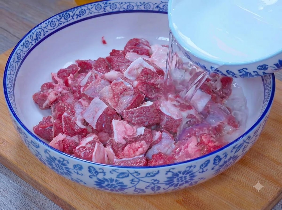 Water pouring from a bowl to submerge beef chunks in a salt and vinegar mixture.
