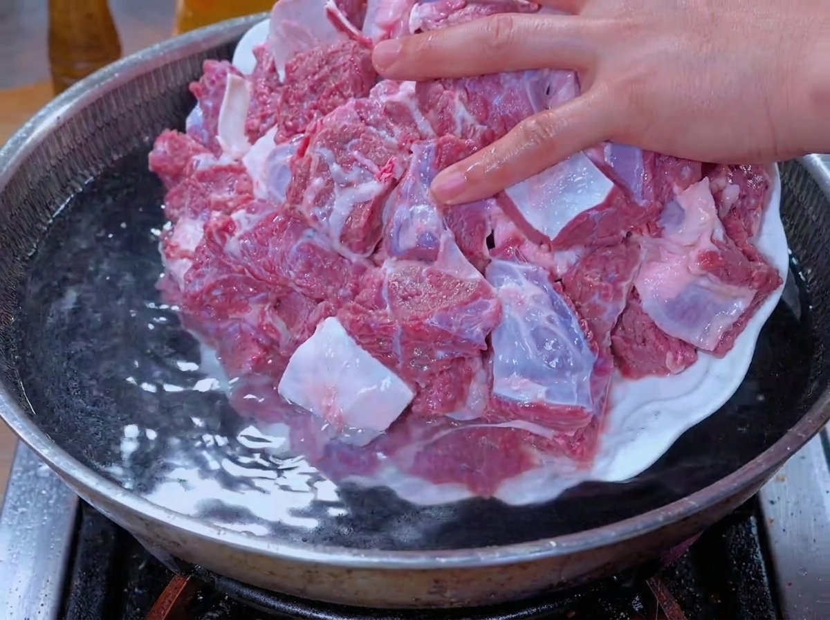 Soaked beef chunks being added to a pot of water for blanching.