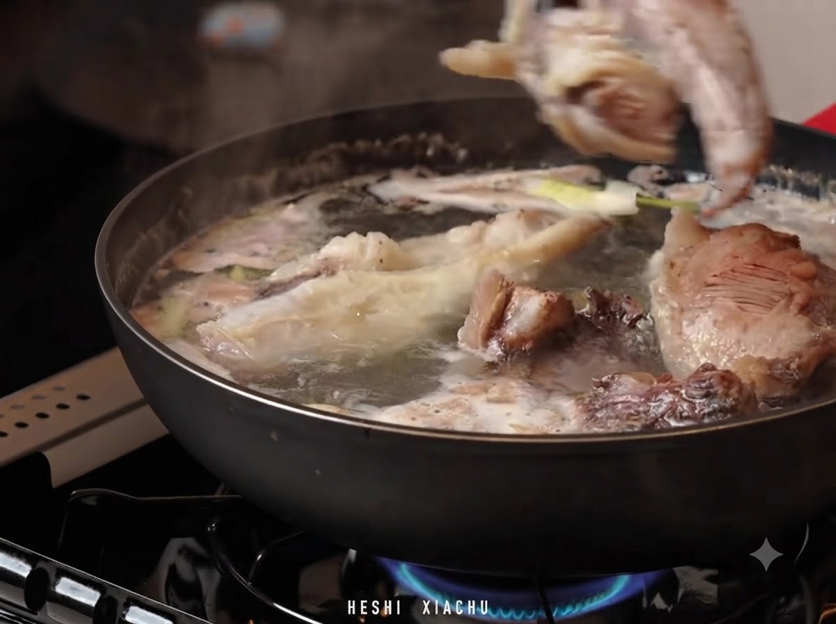 Beef brisket pieces being transferred into a pot of hot water with soup broth and aromatics.