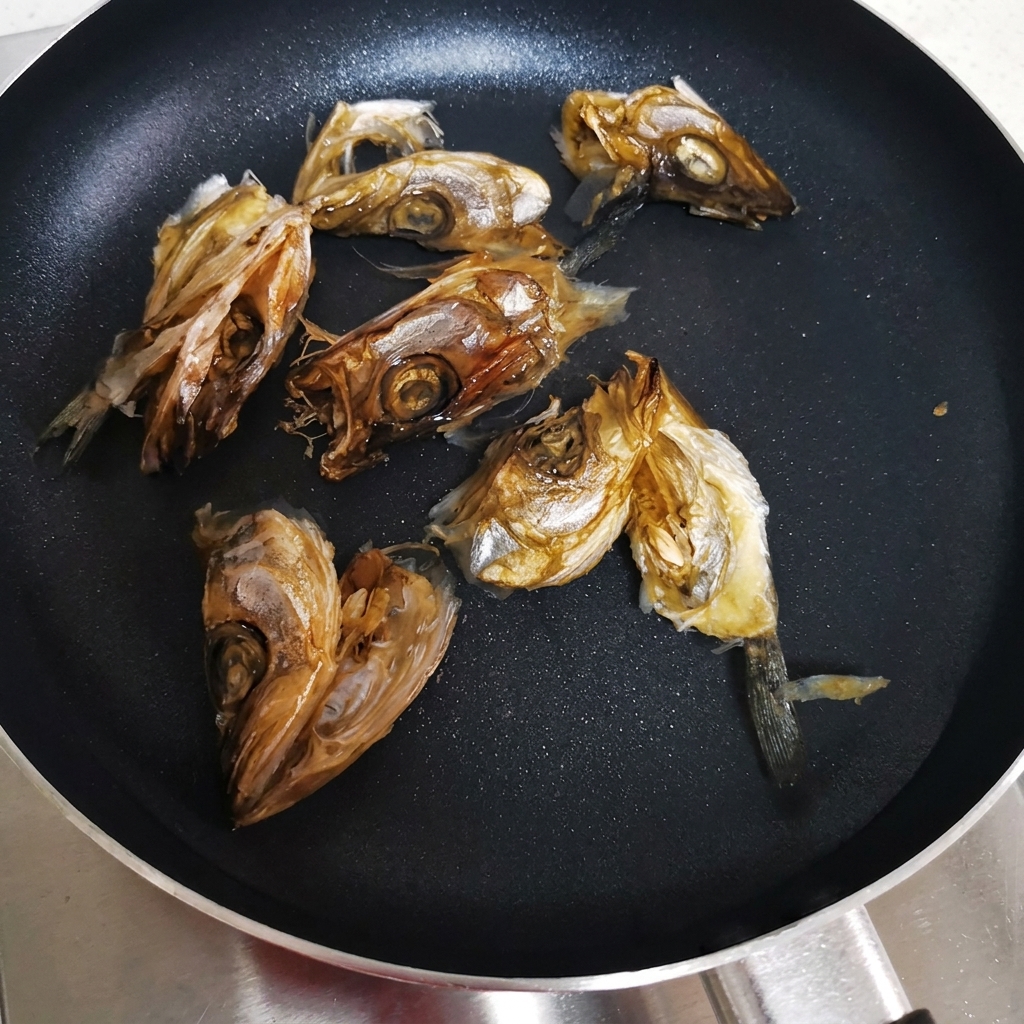 Dried fish heads arranged in a flat pan with cold water ready to be heated.