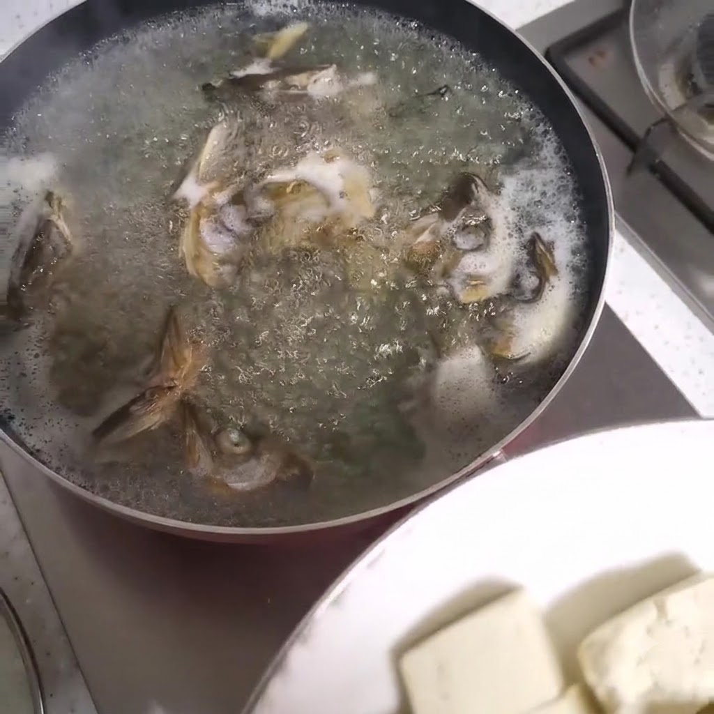 Tofu cubes being added to a bubbling pot of fish head soup.