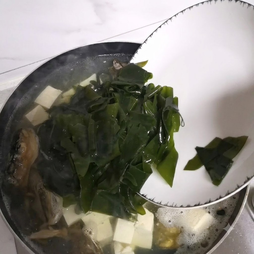 Seaweed pieces sliding from a plate into the simmering pot of soup.